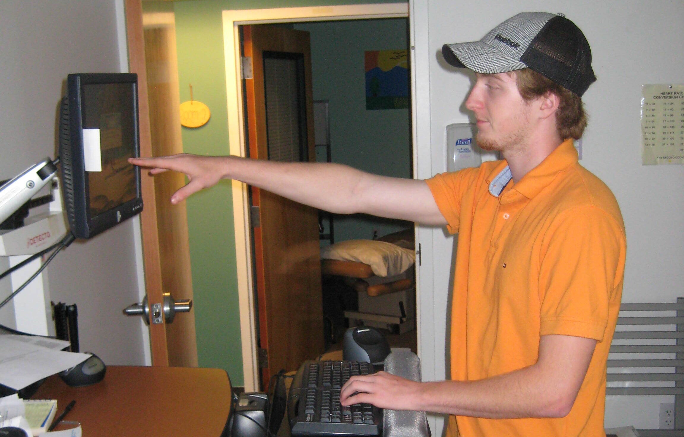 Employee a standing workstation with extended arm assessing the correct ergonomic position for a monitor