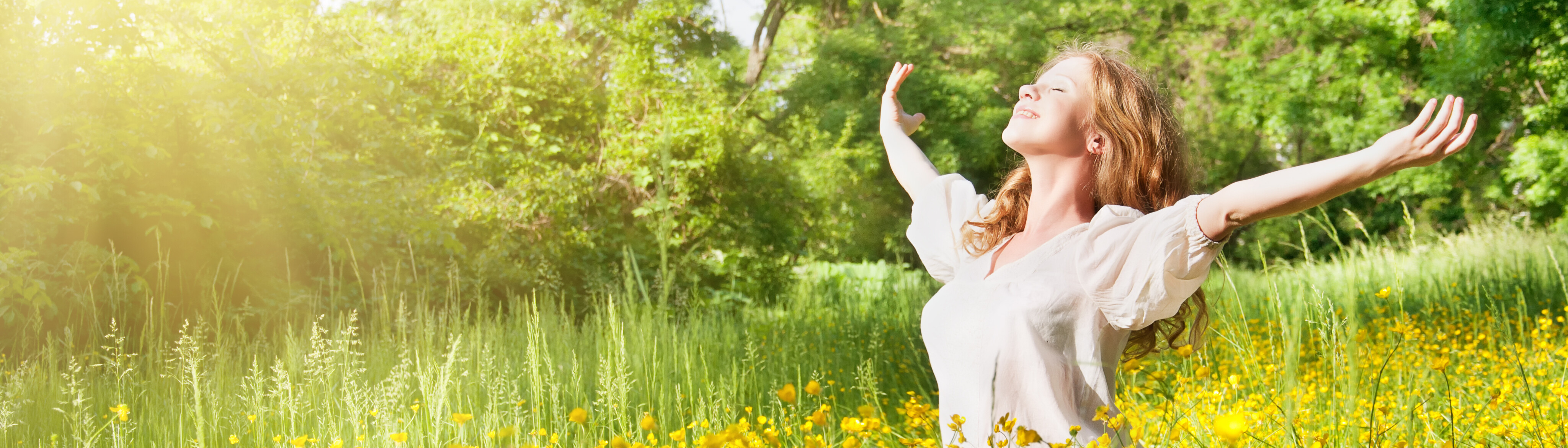 Woman standing in a field of flowers looking upward with outstretched arms